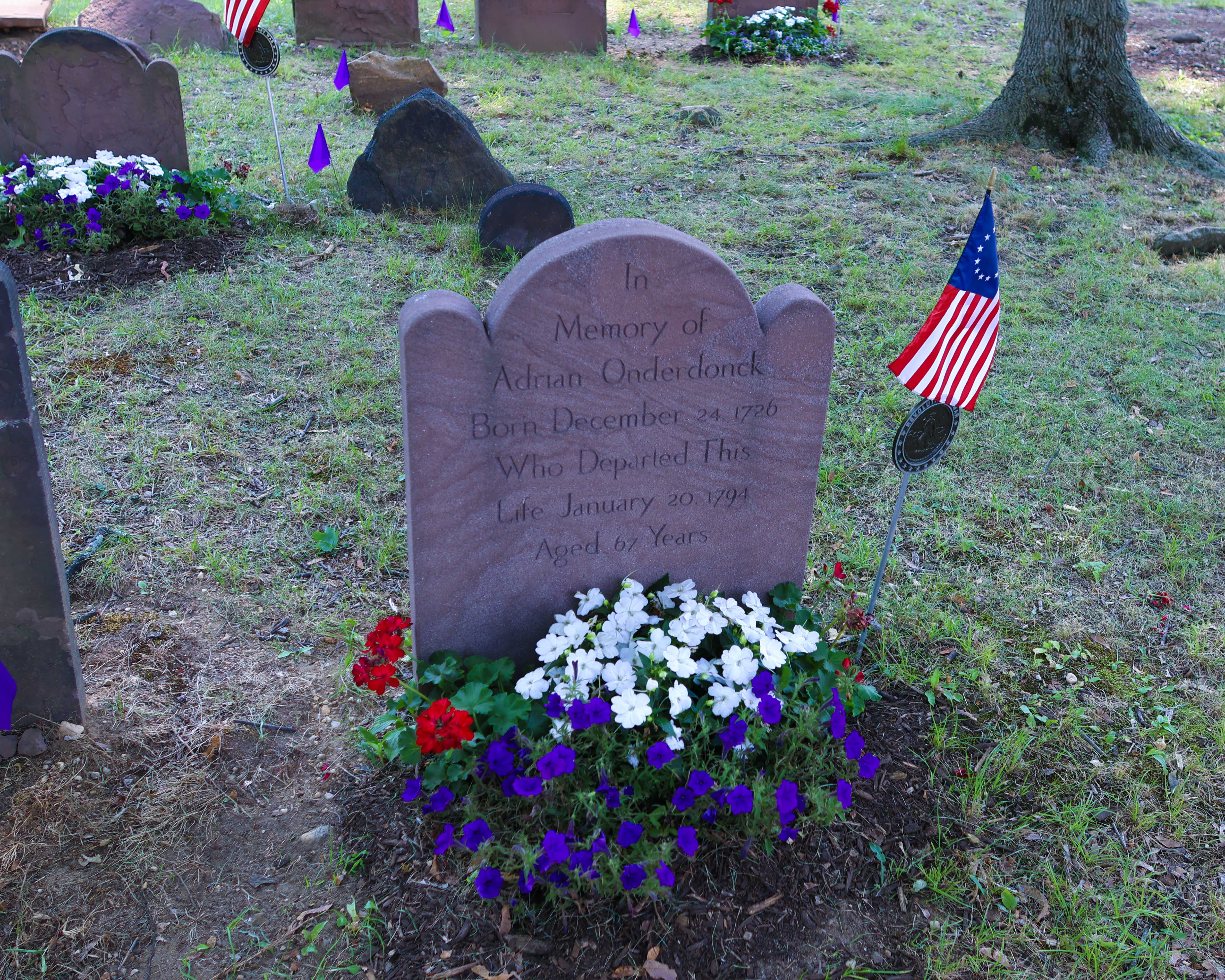 The restored gravestone of Adrian Onderdonk, North Hempstead's first Town Supervisor, adorned with red, white, and blue flowers and a Betsy Ross flag at Monfort Cemetery.