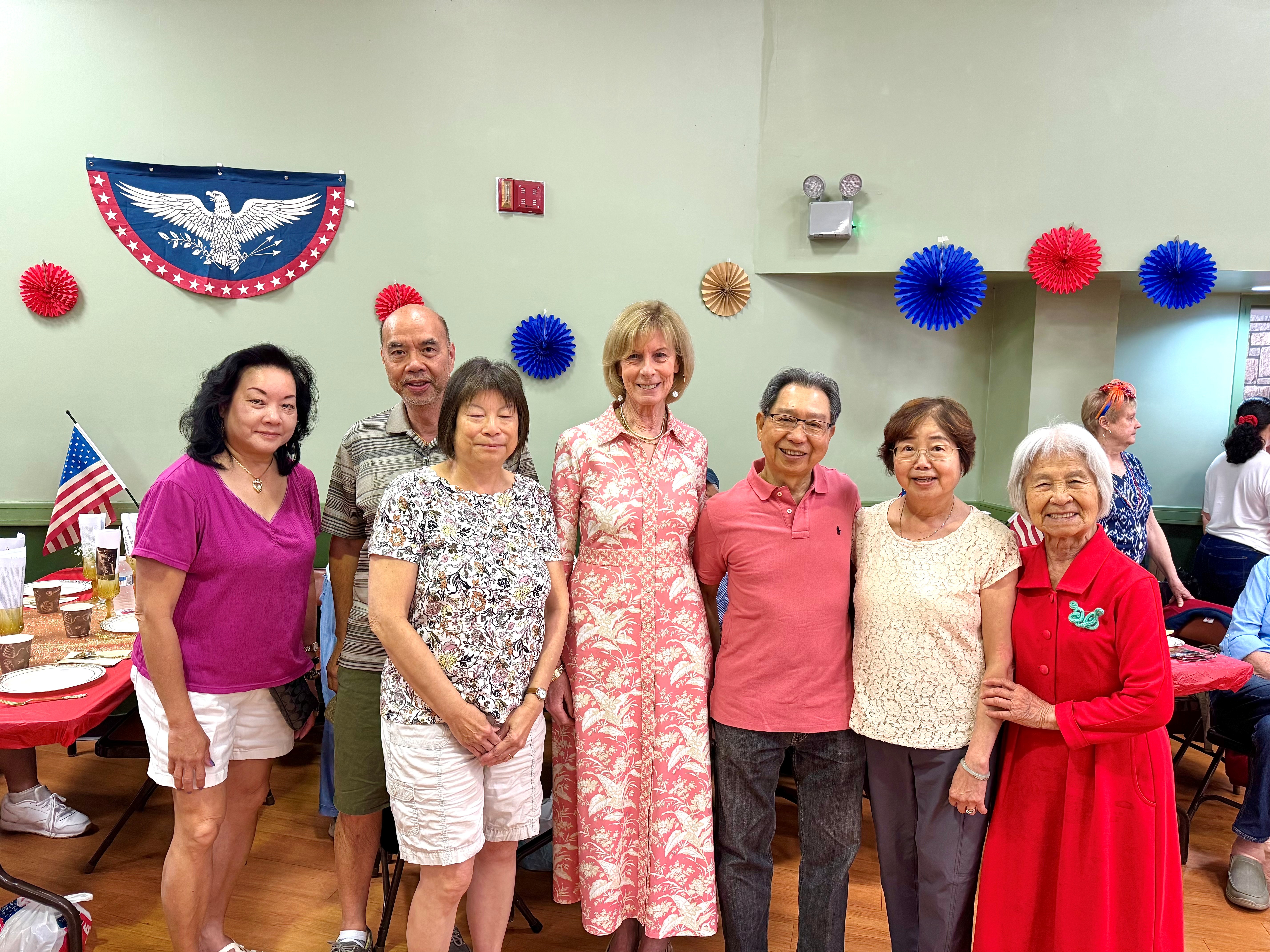 Supervisor Jennifer S. DeSena poses with a group of seniors in front of patriotic decorations, including a half-moon eagle bunting on the wall.