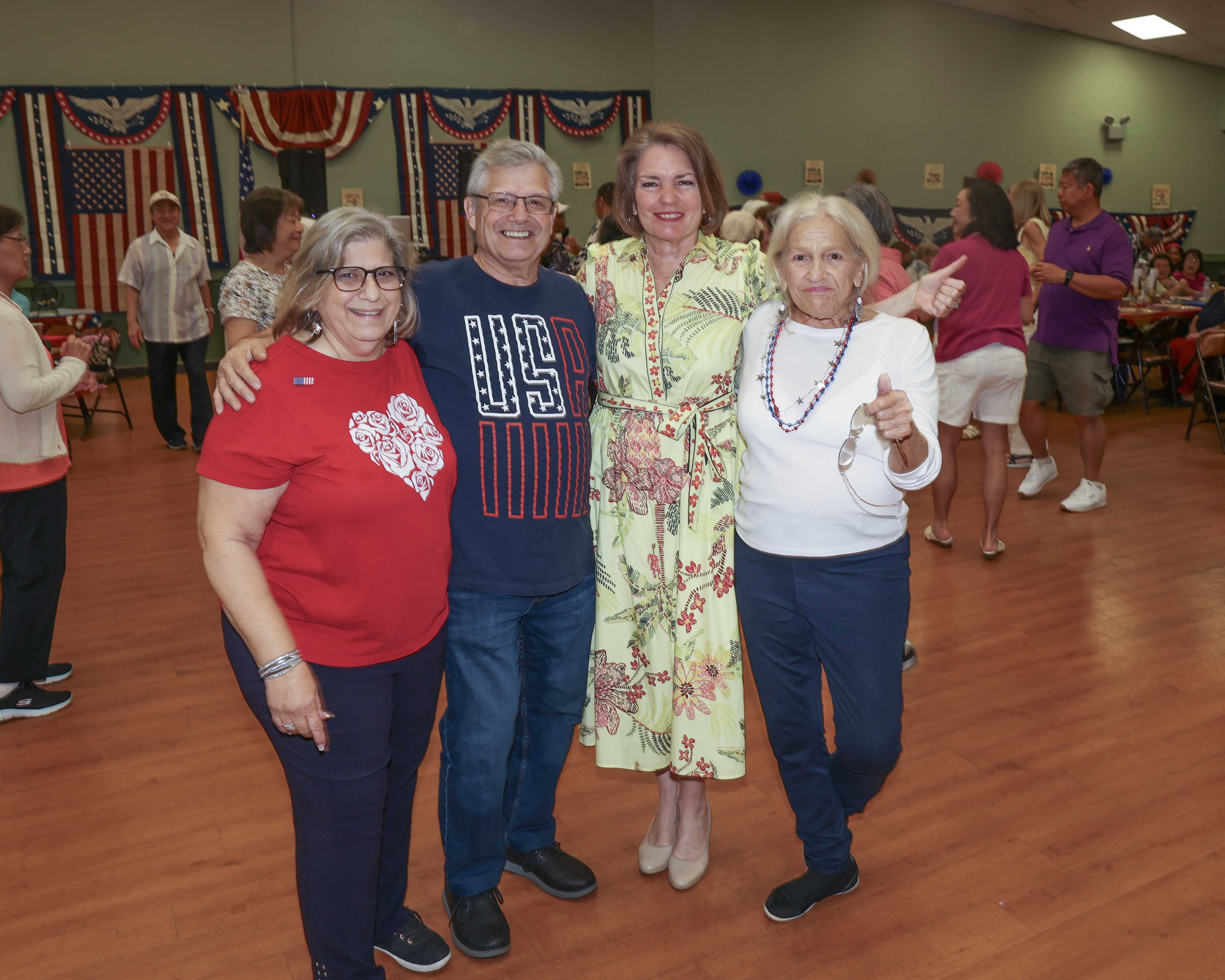 Supervisor Jennifer S. DeSena poses with three seniors on the dance floor, with patriotic bunting and American flags decorating the hall in the background.