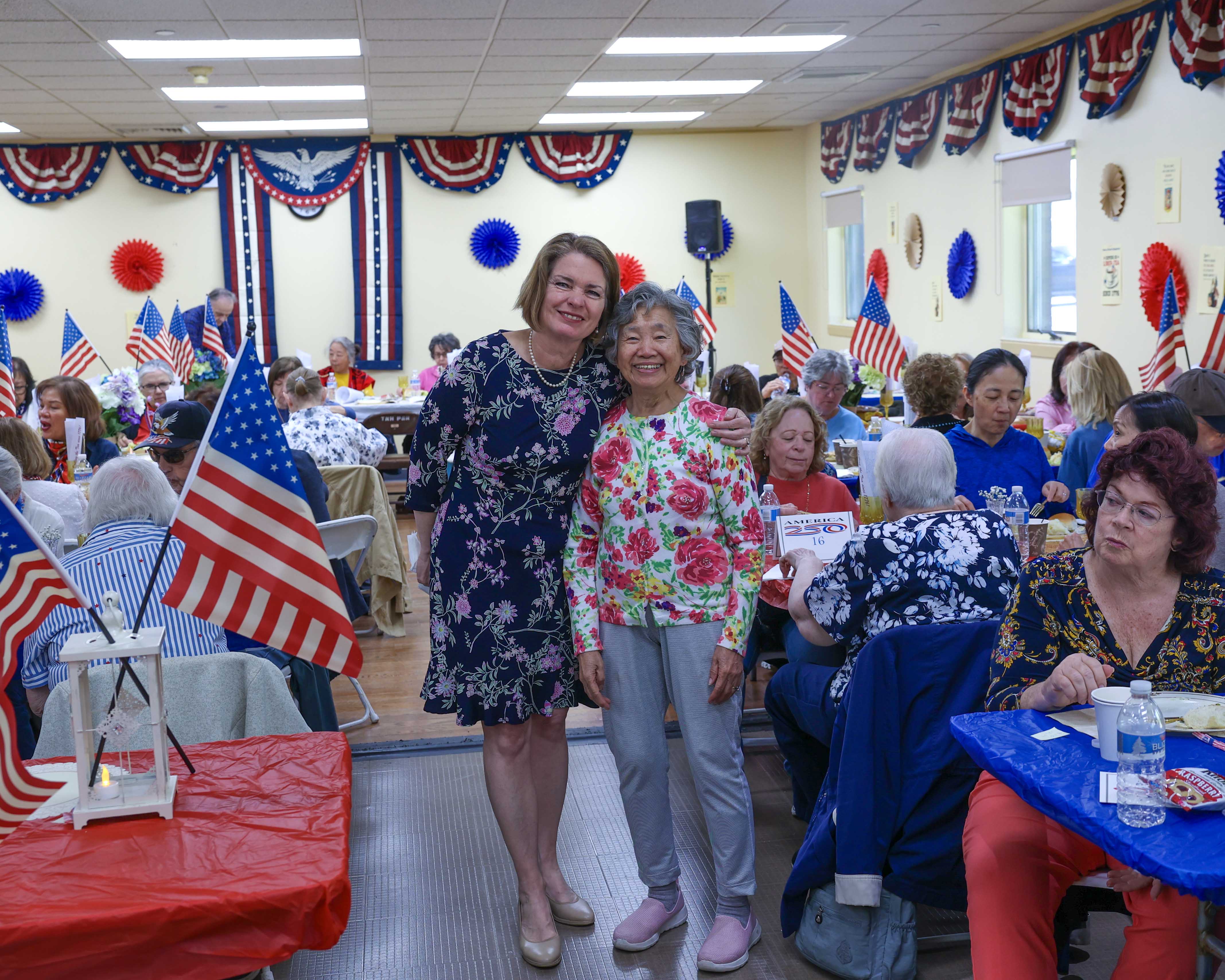 Supervisor Jennifer S. DeSena poses with a senior attendee on the dance floor, with the fully decorated hall and American flags visible throughout.