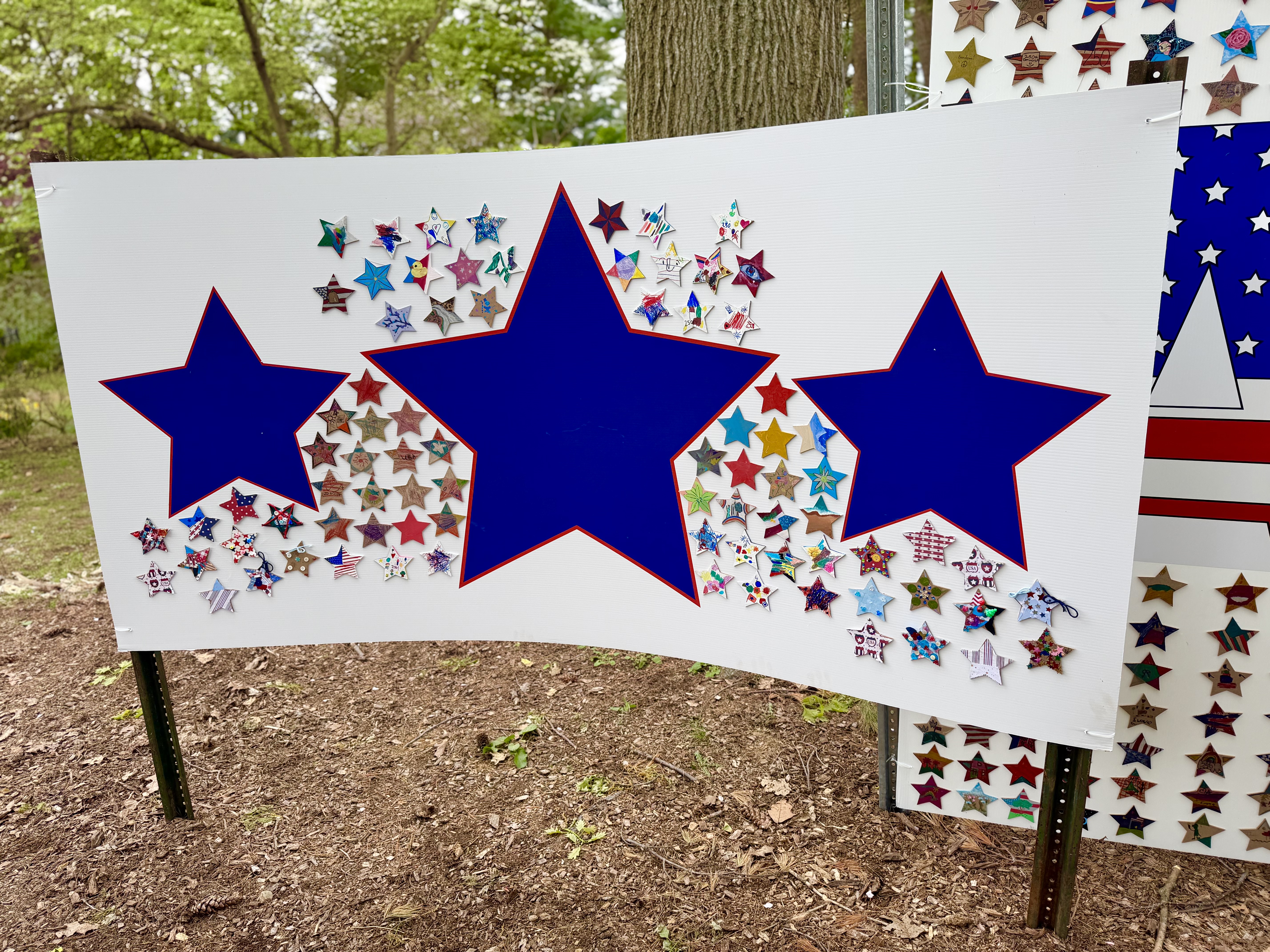 The America 250 student star mosaic on display at Clark Botanic Garden — hundreds of hand-decorated stars by K–12 students arranged around three large navy stars on white panels.