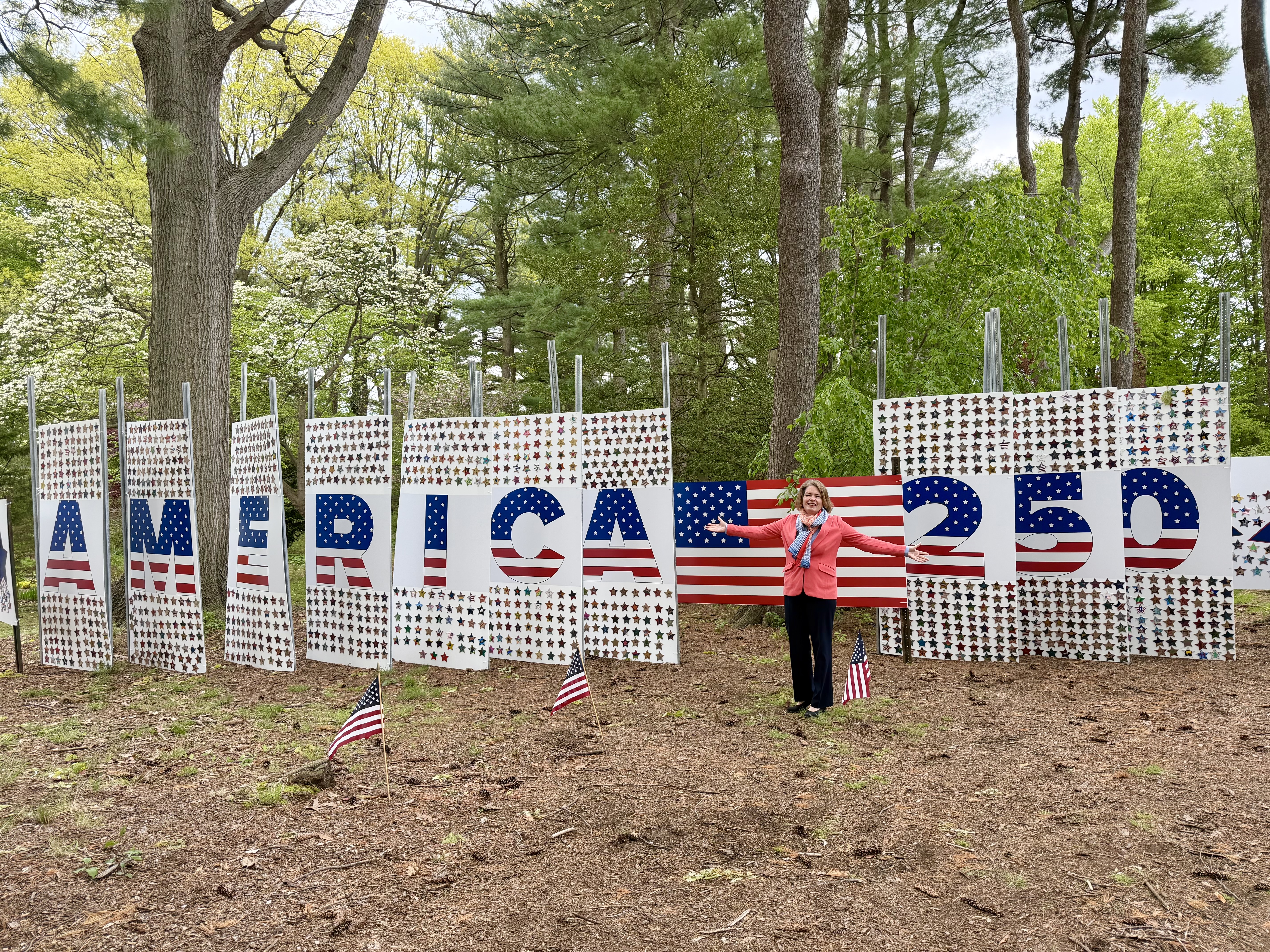 Supervisor Jennifer S. DeSena stands in front of the full America 250 star mosaic installation, which spells out 'AMERICA 250' in red, white, and blue letters covered in student-made stars.